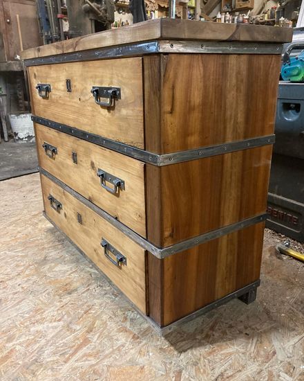 Chest of drawers made out of reclaimed wood, with metal handles and bars between each drawer.