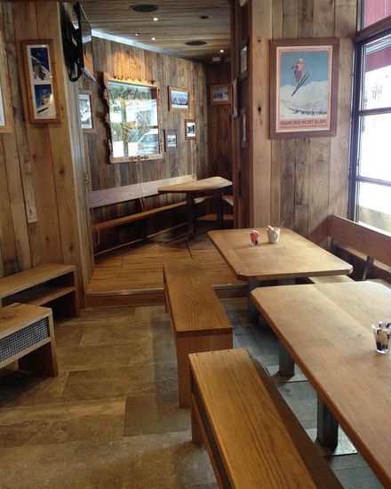 The narrow end of a room with wooden clad walls and ceilings, wooden benches and tables along the walls.