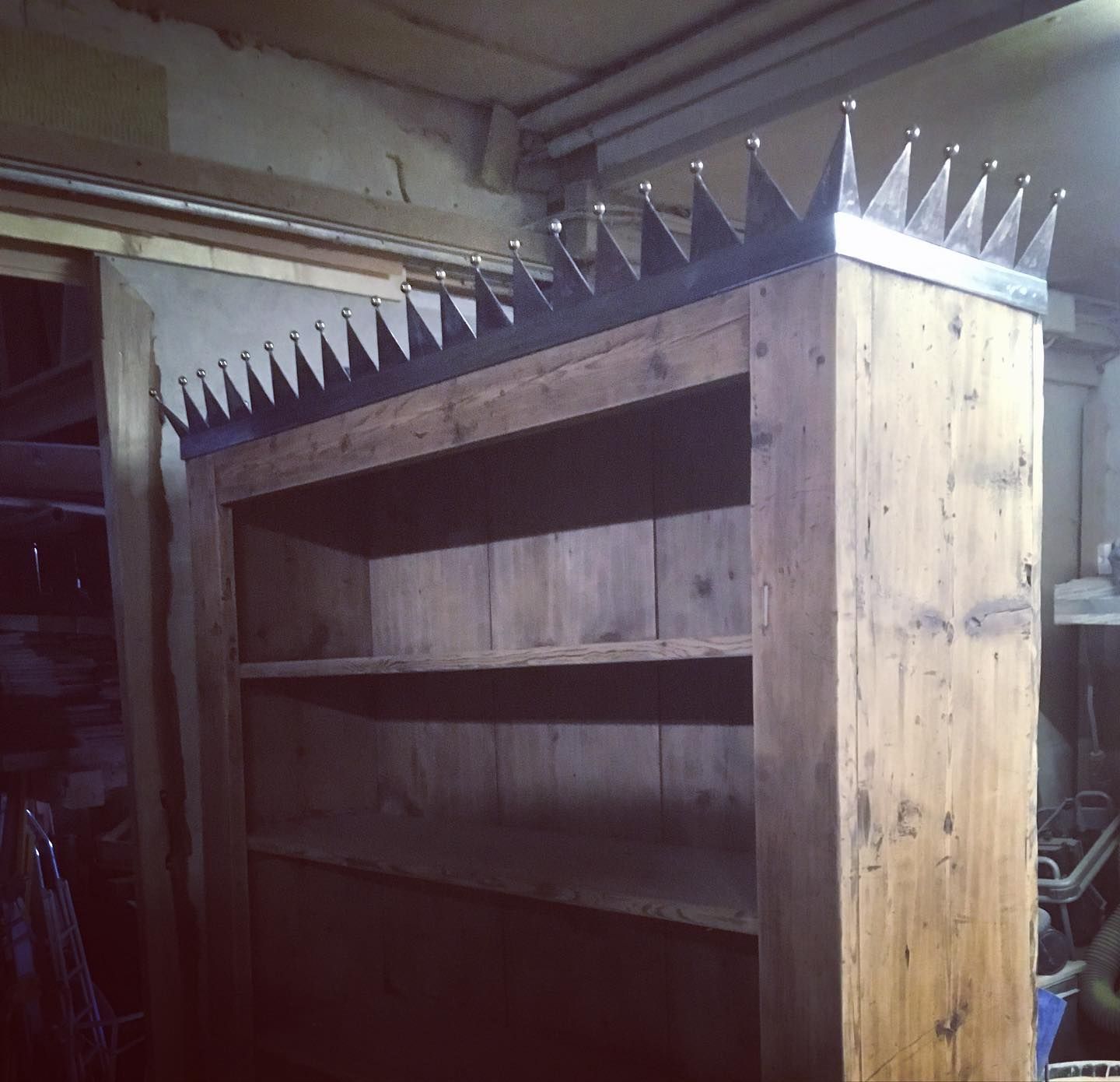 The top half of an old and tall wooden bookshelf, which has attached a metal crown all around the top.