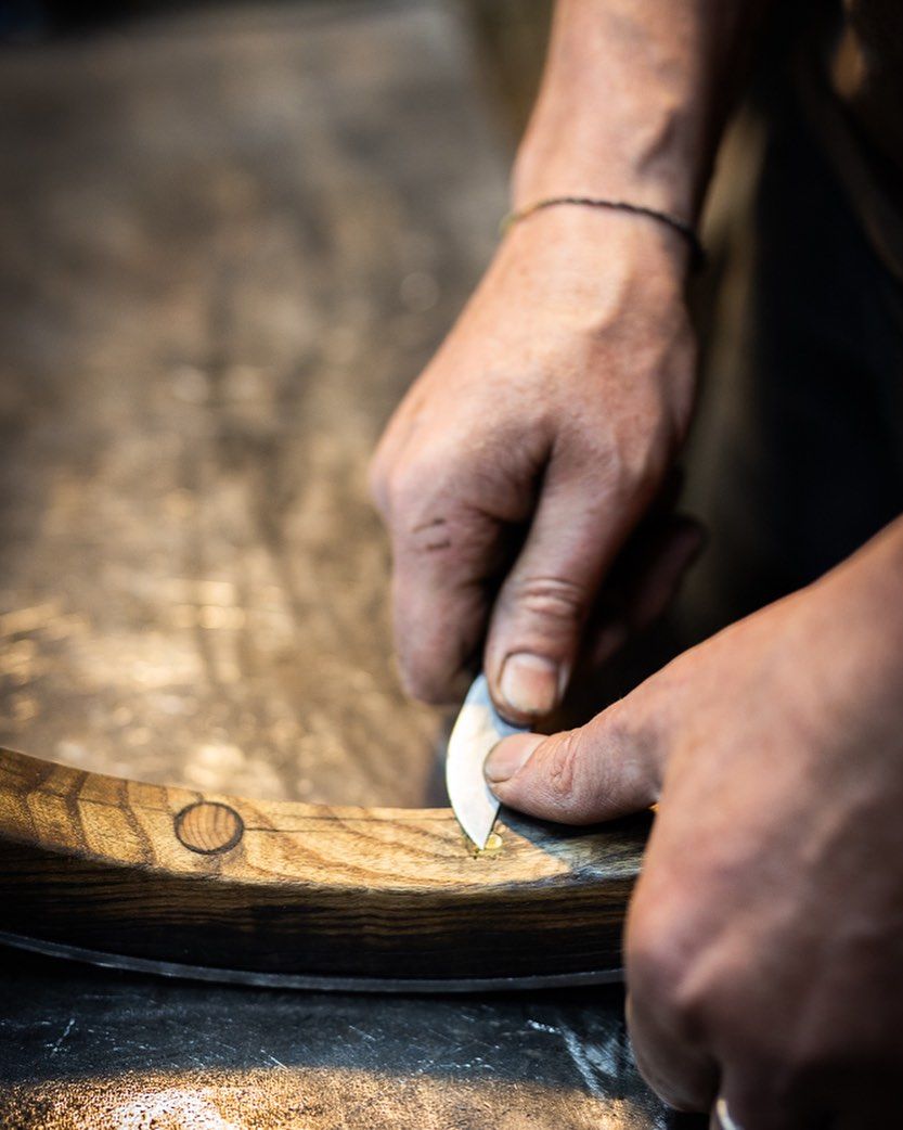 Close-up of hands carefully shaving the edge of a wooden detail with a knife.