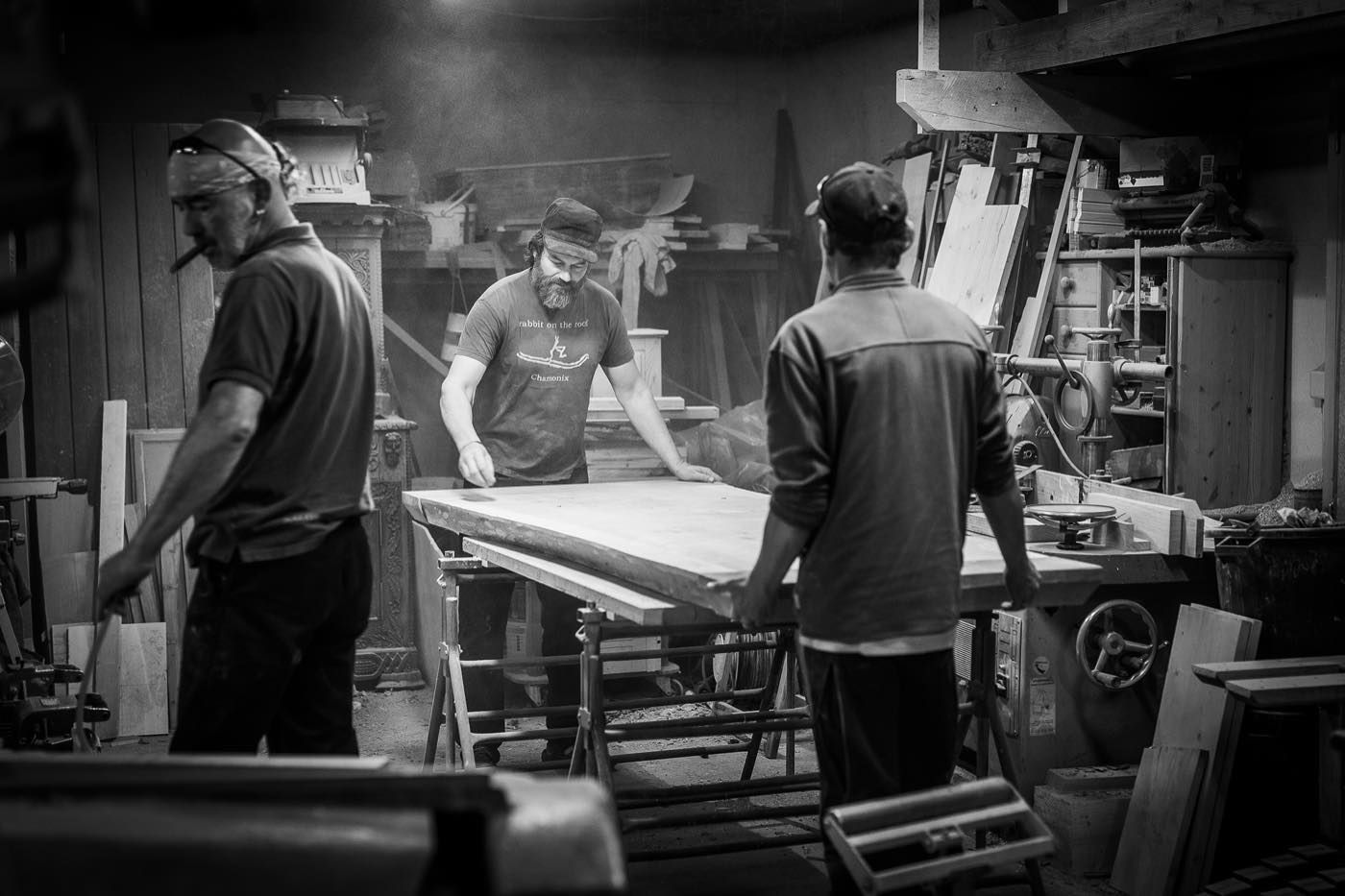 Black and white photo of Jiri and two others working in the workshop, Jiri is focusing on a new table.