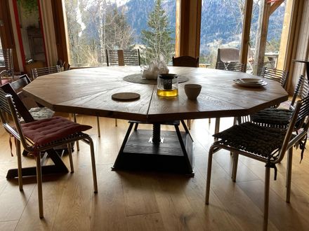 Wooden 10-sided table seen from a lower angle, with chairs around it.